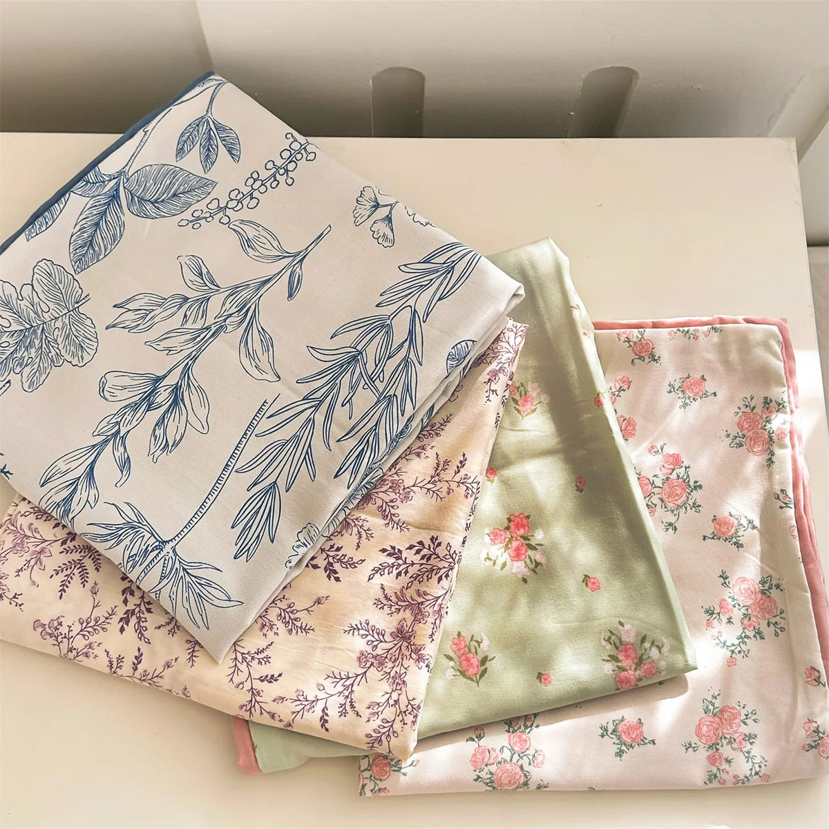 A stack of floral printed pillow covers in shades of pink, green, and white fabric.