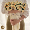 A person holds a hand knitted floral rose bouquet throw blanket against a white blouse and tan pants.