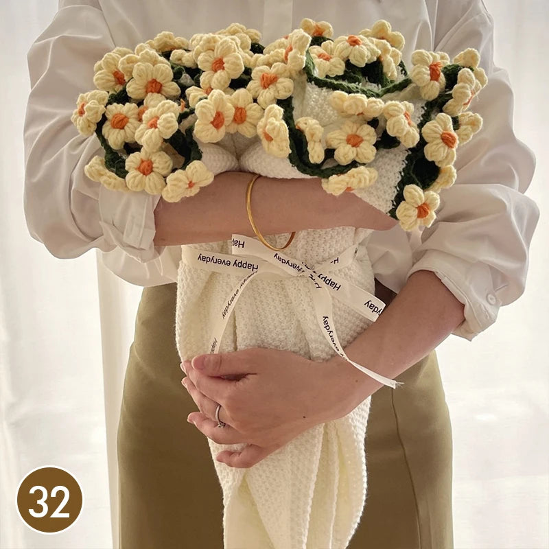 A person holds a hand knitted floral rose bouquet throw blanket against a white blouse and tan pants.