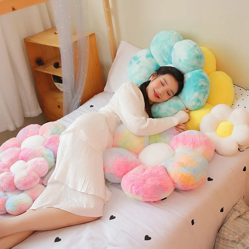 A person is lying on a bed surrounded by numerous soft, pastel-colored sunflower plush flower cushions.