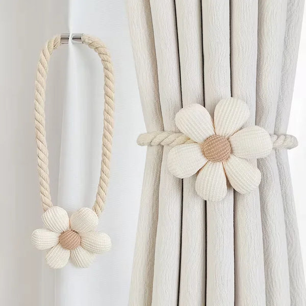 A pair of beige magnetic floral curtain tiebacks with braided cord.