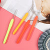 A set of three orange and yellow aluminum plastic crochet hooks displayed on a pink background.