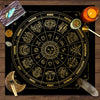 A circular gold-on-black tarot chart with twelve zodiac signs and planetary symbols, set on a wooden surface.