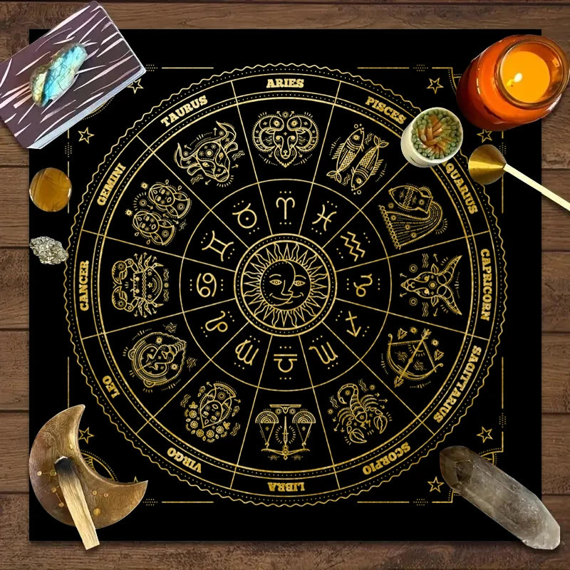 A circular gold-on-black tarot chart with twelve zodiac signs and planetary symbols, set on a wooden surface.