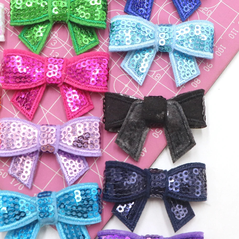 A collection of colorful sequin bow patches and ribbons for DIY decoration displayed on pink paper.