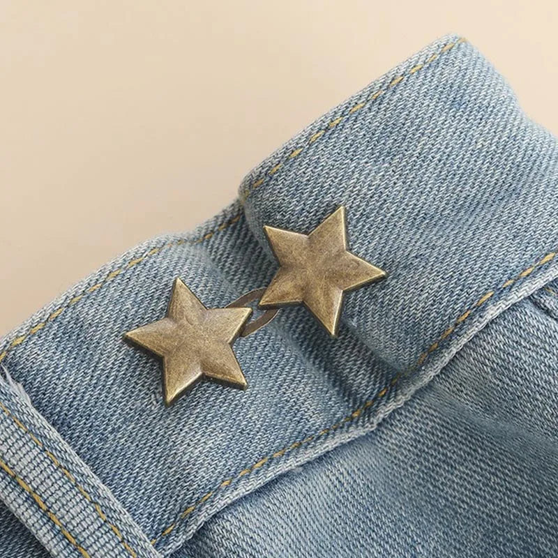 Two gold star-shaped brooches pinned onto a blue denim fabric