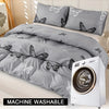 A gray duvet cover with a black butterfly print is displayed next to a white washing machine.