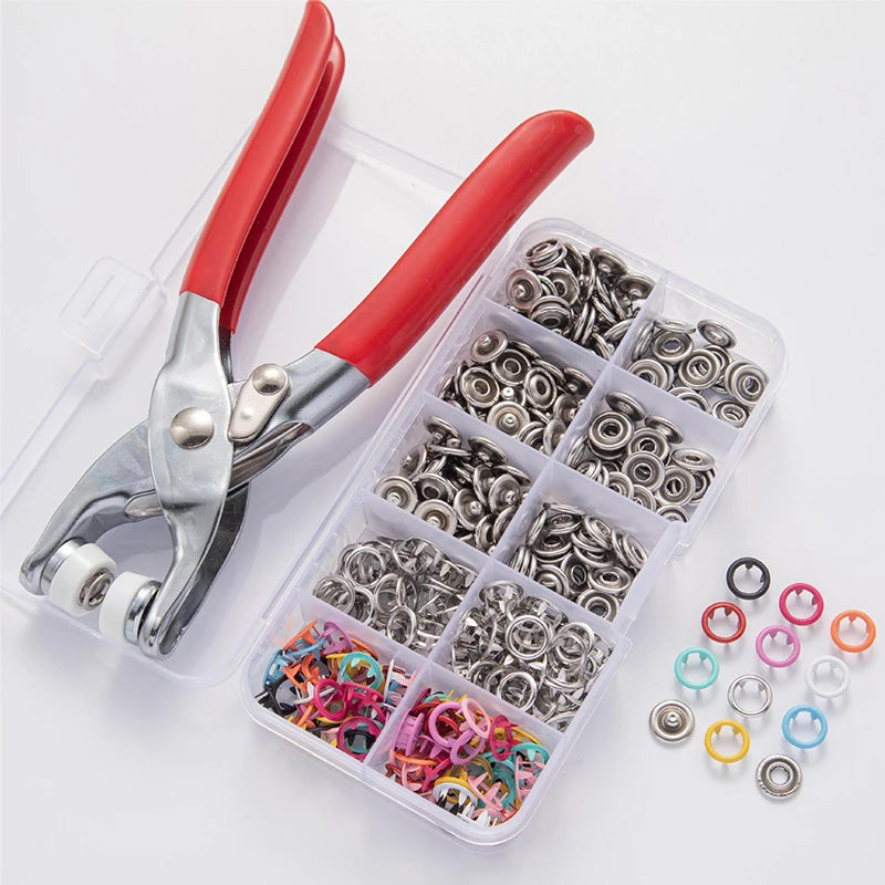 A pair of red-handled pliers holding a clear plastic case filled with various metal snap buttons and rings.