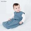 A baby wearing a blue muslin cotton sleeping bag is lying down on a white surface.