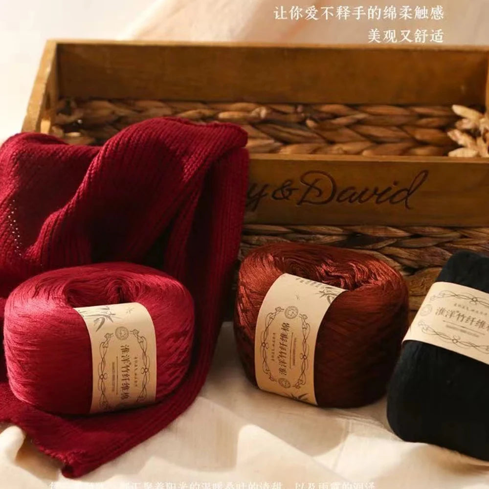 A stack of deep red yarn rolls and a folded red scarf are displayed in a wooden box with straw bedding.