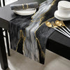 Black and gold abstract marble linen table runner displayed on a dark table with white plates.