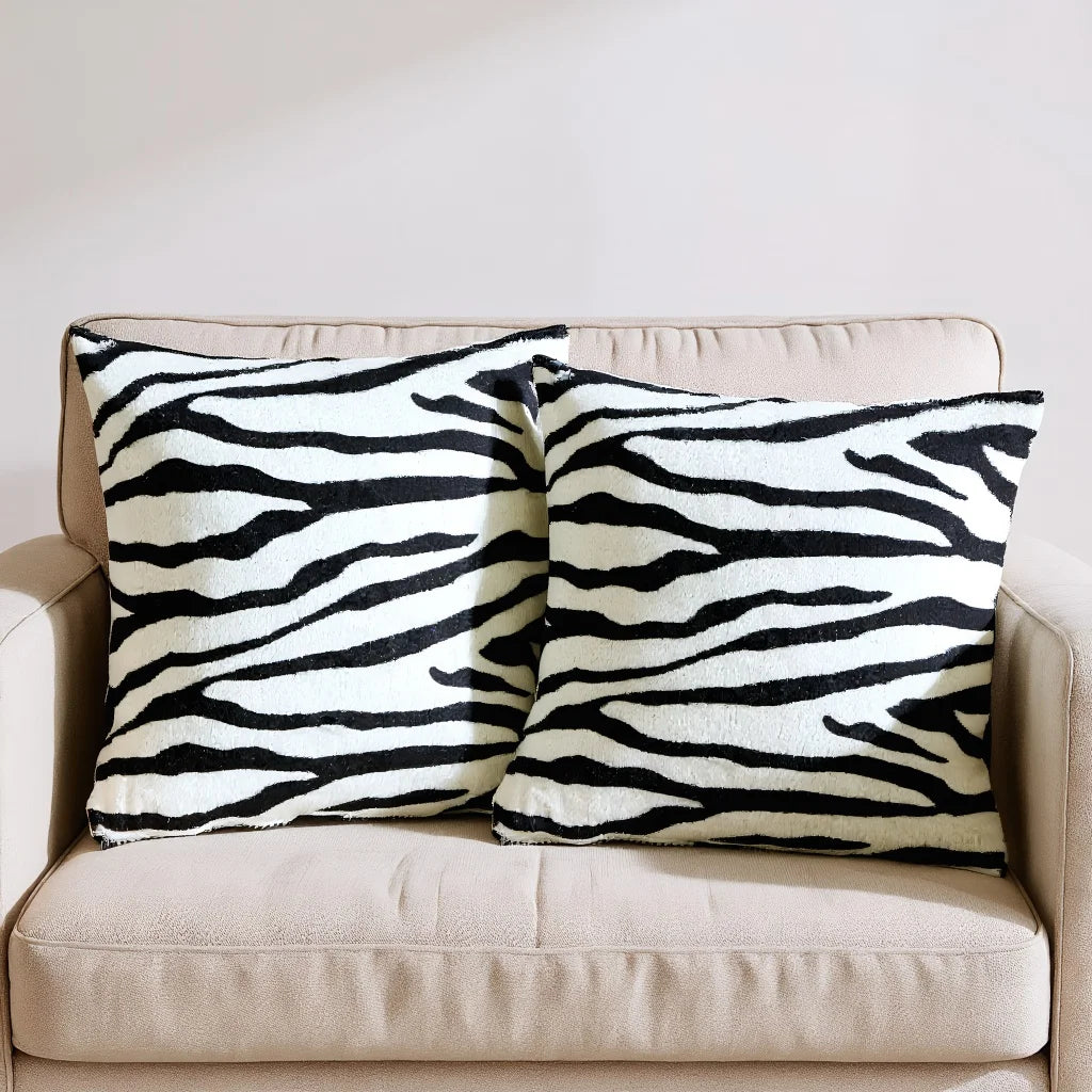 Two throw pillows with a black and white leopard print pattern resting on a beige sofa.