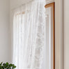 White sheer curtains with floral lace detailing hanging in a wooden frame.