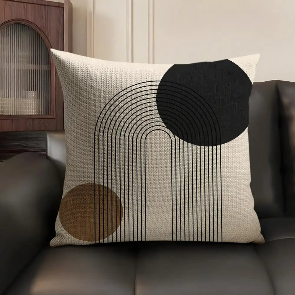 A beige cushion cover featuring black geometric lines and circles on a dark brown leather sofa.