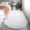 A fluffy white plush floor mat placed on a light gray floor with a potted plant and books nearby.