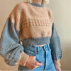 A person is wearing a knitted sweater with beige, gray, and tan sections over a denim shirt.