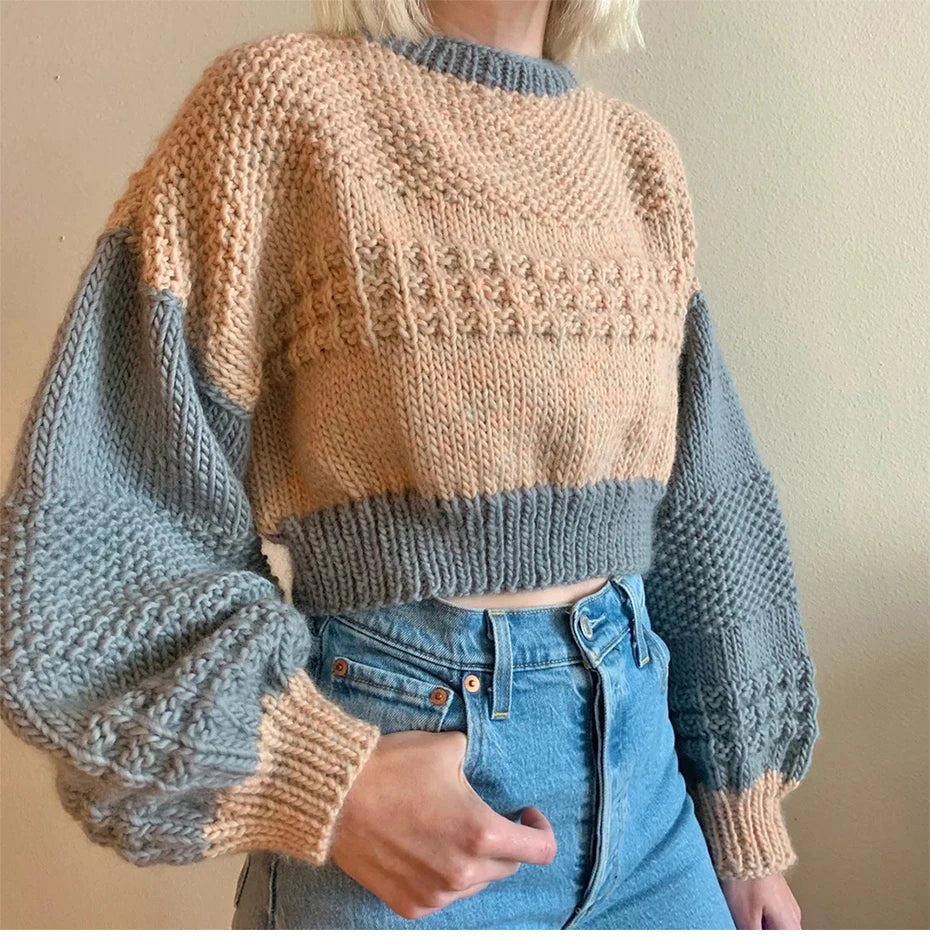 A person is wearing a knitted sweater with beige, gray, and tan sections over a denim shirt.