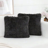 A set of two dark gray faux fur throw pillows resting on a white surface next to a framed picture.