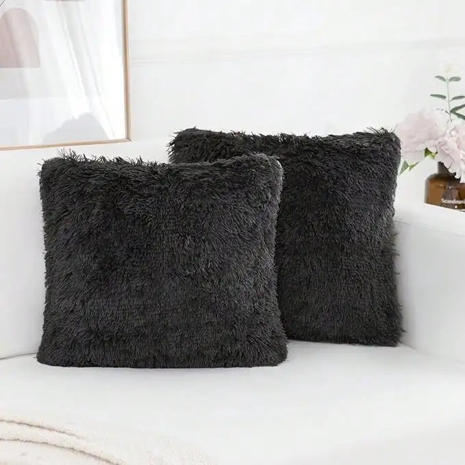 A set of two dark gray faux fur throw pillows resting on a white surface next to a framed picture.