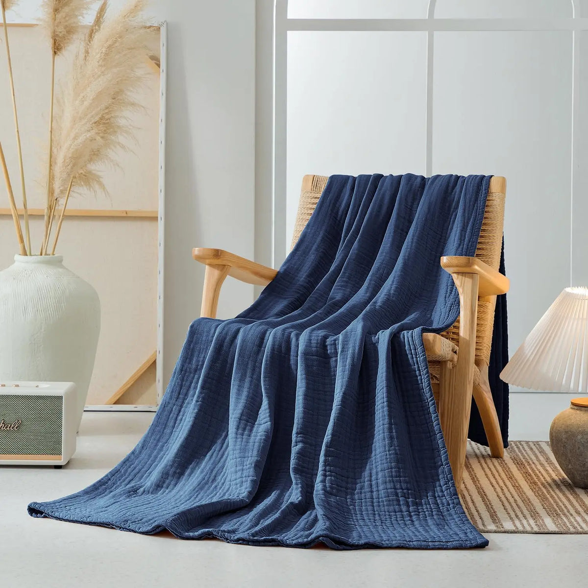 A deep blue muslin blanket draped over a wooden chair in a bright, minimalist room.