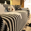 A close-up of a white and black patterned chenille sofa cover with a spherical white tassel decoration.