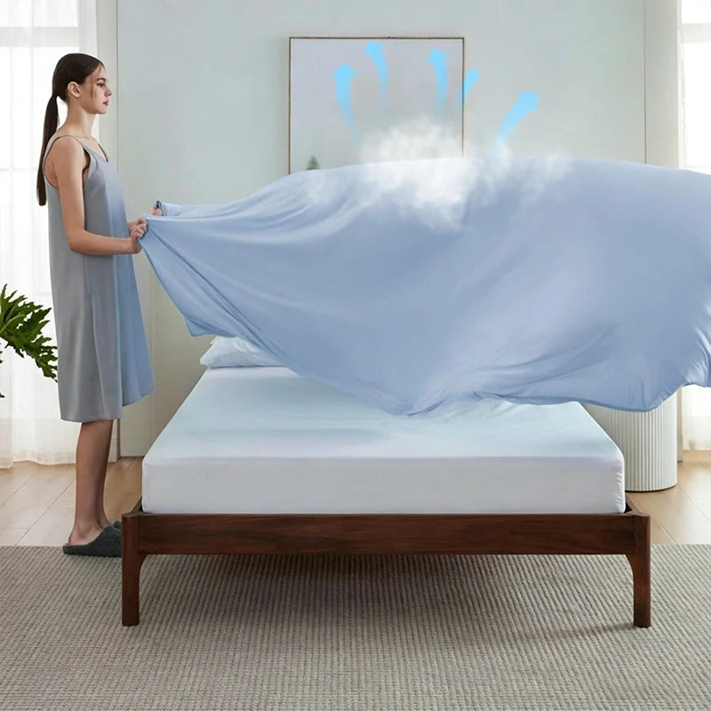 A light blue ice silk cooling blanket is draped over a white bed in a bright room.