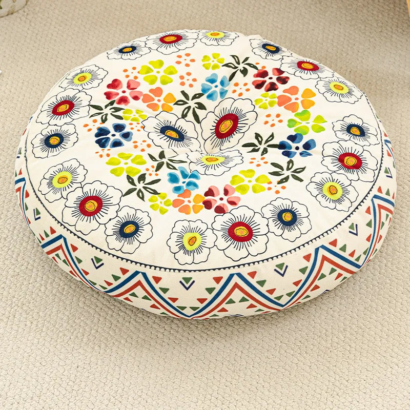 A round cushion with a floral pattern featuring colorful flowers and leaves, suitable for floor seating.