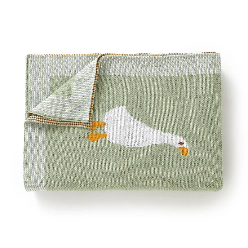 A light sage green cotton blanket with a white goose or duck print and a ribbed edge.