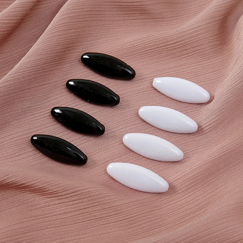 Eight plastic safety pins in black and white oval shapes arranged on a pink fabric.