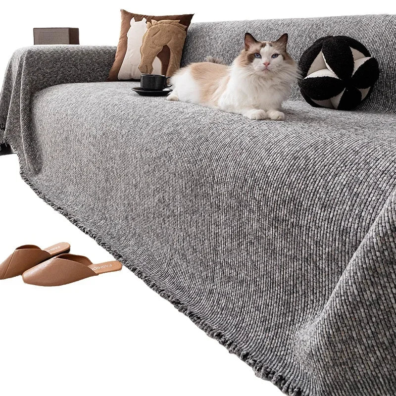 A fluffy ginger and white cat is relaxing on a gray sofa cover with pillows and a black decorative ball.