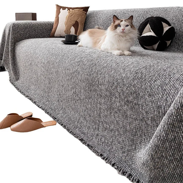 A fluffy ginger and white cat is relaxing on a gray sofa cover with pillows and a black decorative ball.