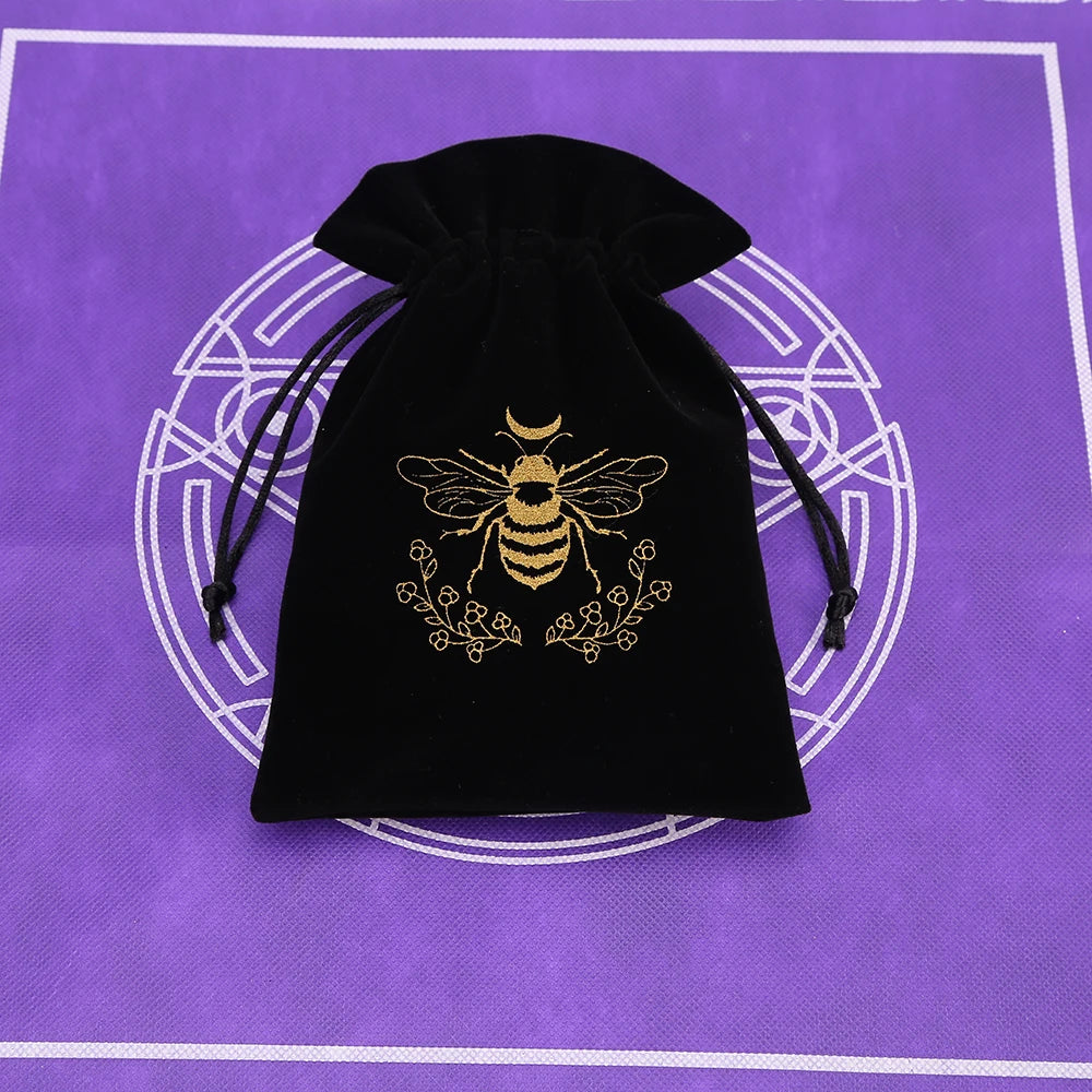 Black velvet pouch with a gold bee emblem resting on a purple surface.