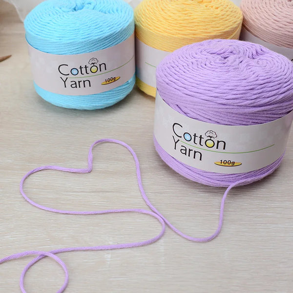 A collection of skeins of colored cotton yarn, including blue, yellow, and purple, displayed on a light wooden surface.