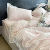 A pink gingham plaid duvet cover and pillowcase set with white lace trim on a bed.