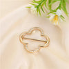Gold-toned metal ring clips shaped like leaves or hearts, set against a soft cream fabric with white flowers.