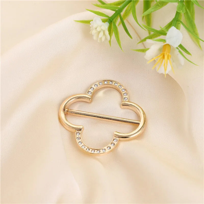Gold-toned metal ring clips shaped like leaves or hearts, set against a soft cream fabric with white flowers.