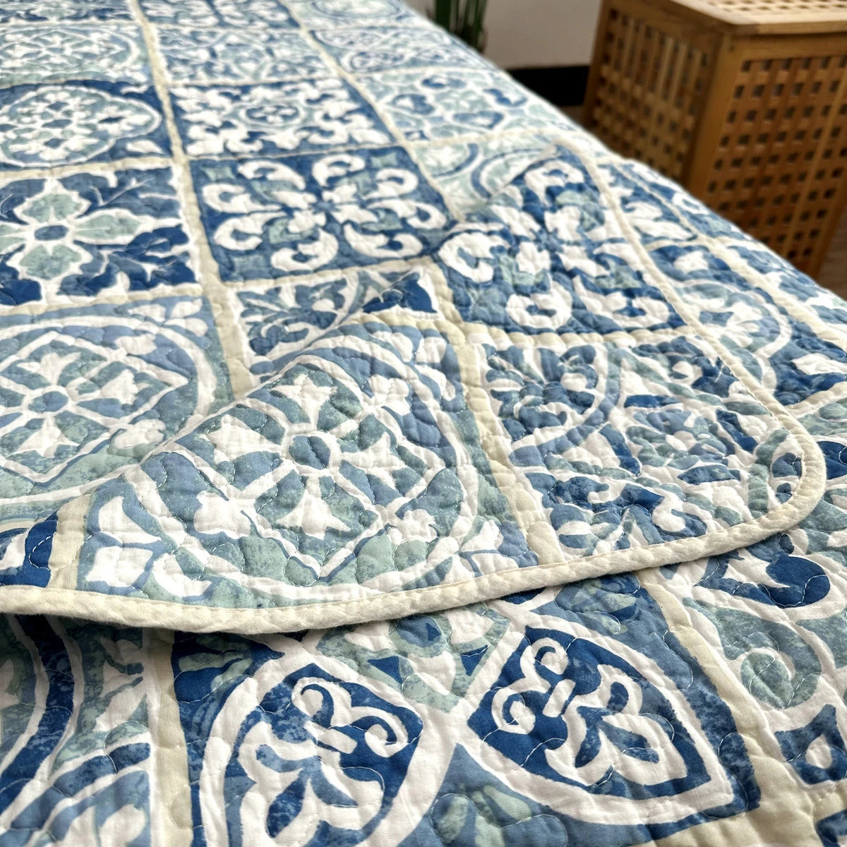 A blue and white pastoral embroidered cotton quilted bedspread with a diamond pattern.