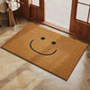 A rectangular, tan coconut fiber doormat with a simple black smiling face placed on a light wood floor near a glass door.