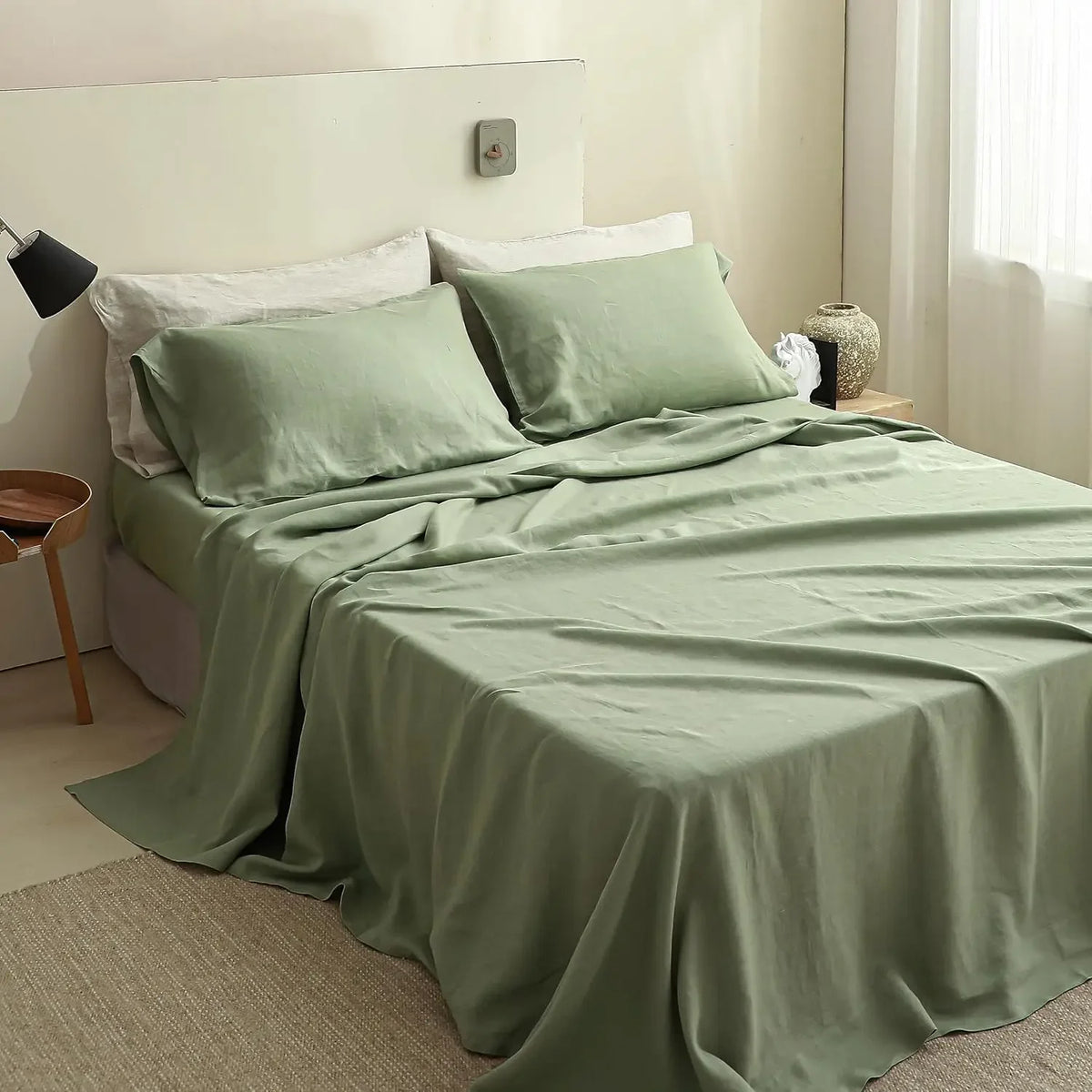 A light sage green French stone washed linen bedding set with white pillows and a matching duvet on a bed.