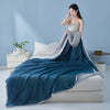 A deep teal quilt draped over a white bed, with a model wearing a light top standing beside it.