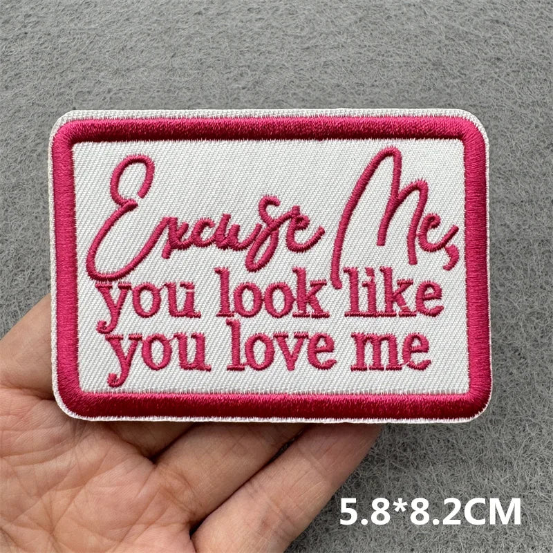 Pink embroidered slogan patch with script text on white fabric shown being held by a hand
