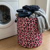 A pink leopard print foldable laundry basket filled with dark clothing and towels.