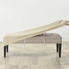 A beige velvet bench slipcover stretched over a upholstered bench with visible securing straps.
