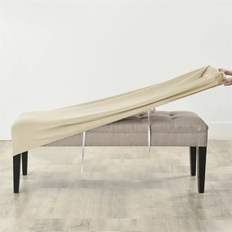 A beige velvet bench slipcover stretched over a upholstered bench with visible securing straps.