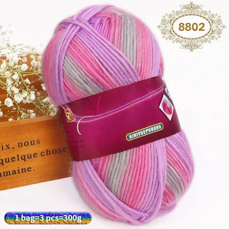 A skein of gradient pink and gray wool yarn is shown next to a wooden box.