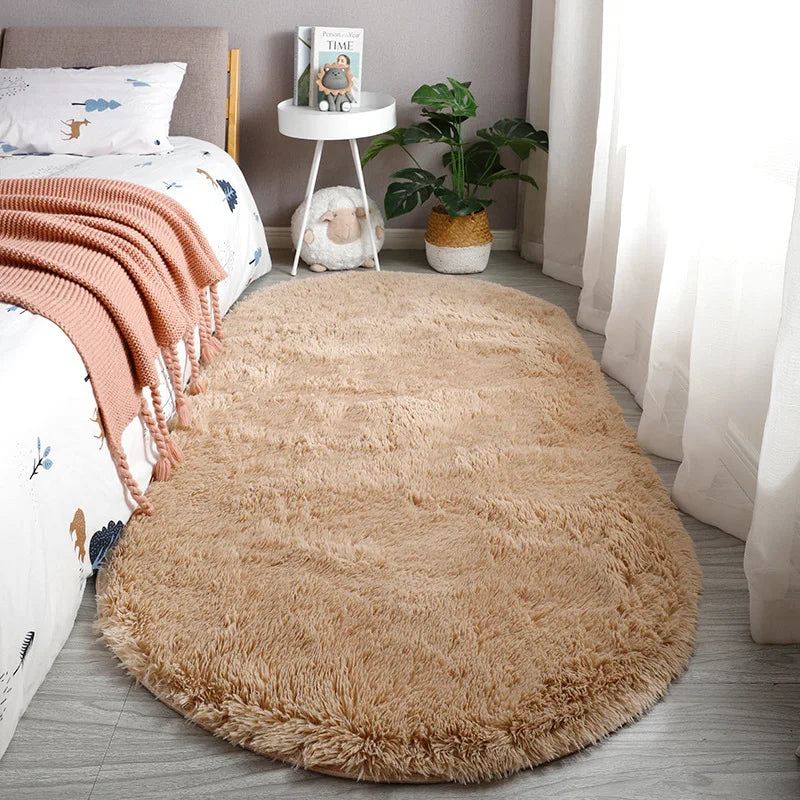 A fluffy beige plush floor mat placed in a light gray room with a bed and potted plant.