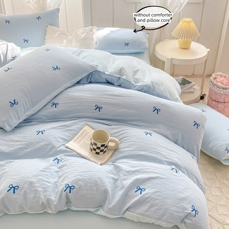 A light blue duvet cover set with pink bowknot embroidery and a matching pillow core displayed on a bed.