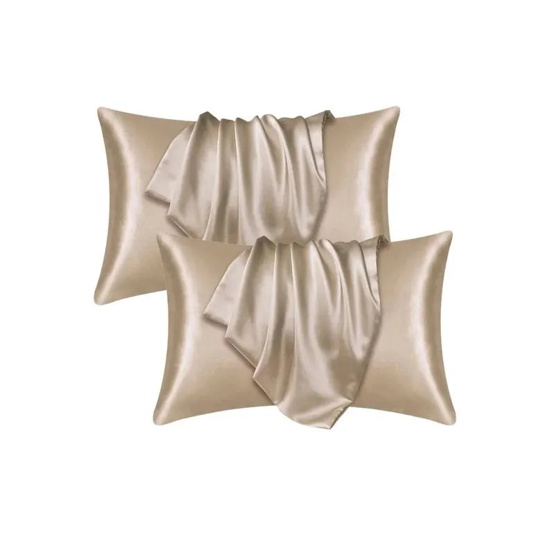 A set of two satin silk pillow covers in a champagne or beige color, draped and folded.