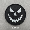 A black circular patch featuring a white stylized skull face with sharp teeth.