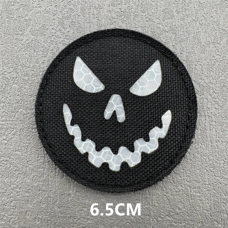 A black circular patch featuring a white stylized skull face with sharp teeth.